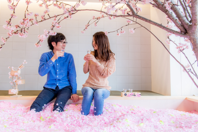 A couple sitting on the edge of a large indoor tub filled with cherry blossoms